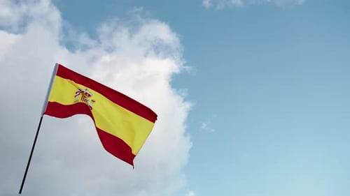 Spanish Flag Waving Against Blue Sky and Clouds