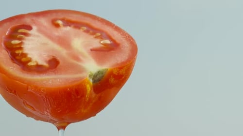 Half of a red tomato, water dripping from it, against a blue sky, close-up