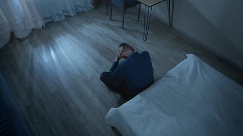 Lonely man sitting on the floor in a dark room in a state of despair and depression.