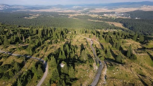 The car drives along a beautiful mountain road, around the forest and epic mountains. Aerial view.