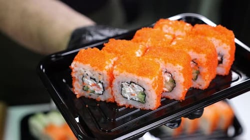 A Closeup Chef in Gloves Holds a Plate of Sushi in the Restaurant's Kitchen
