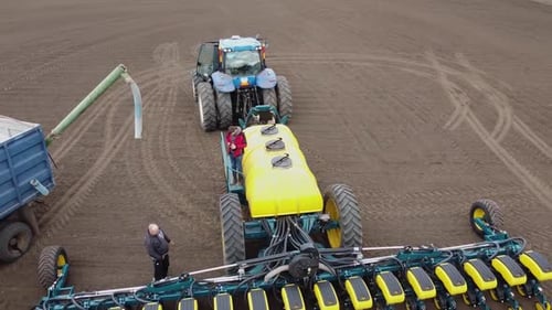 Blue tractor with yellow seeder working on the field in Ukraine OA