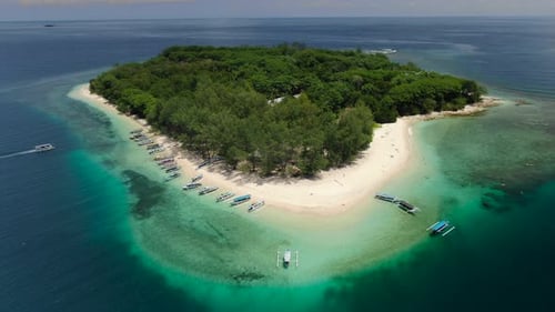 Aerial ascending shot of a tropical island in the middle of the ocean. Traditional Jukung boats on a