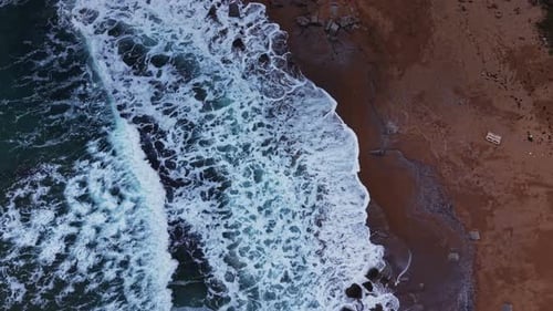 Waves crash on sandy beach near rocky shore during sunny day