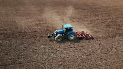 Aerial view of a tractor with harrow plowing a field before planting a crop.