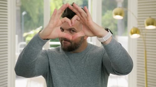 Adult Man Makes Heart Shape with Hands Indoors