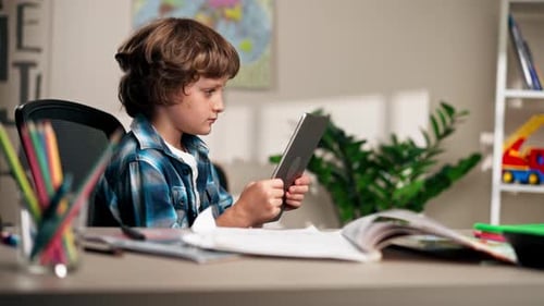 in the Children's Room a Schoolboy in a White Sweater and a Blue Checkered Shirt at a Desk Does