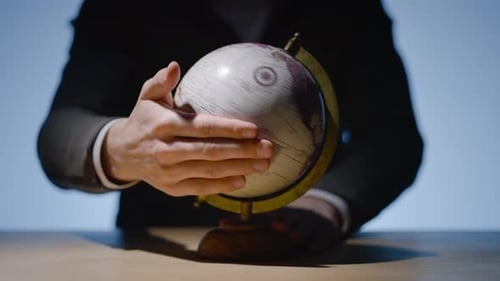 Closeup of a Man's Hand Rotating a Globe and Pointing His Finger at a Country to Visit