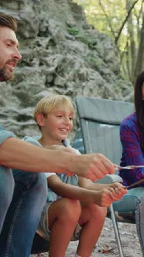 Smiling Family Father Mother and Son Daughter Roast Sausage Over Campfire During Picnic in Forest