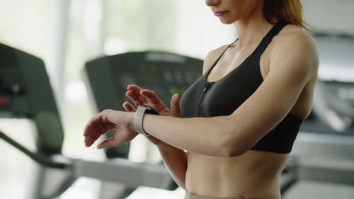 A Young Girl Athlete in the Gym Uses a Fitness Watch to Check Her Pulse and Regulate Physical