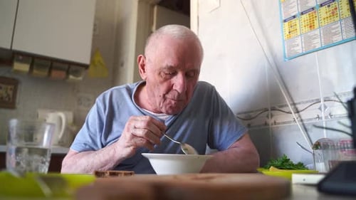 Elderly Senior Man Eating Soup with Bread and Green Onion at Home in the Kitchen Happy Retirement