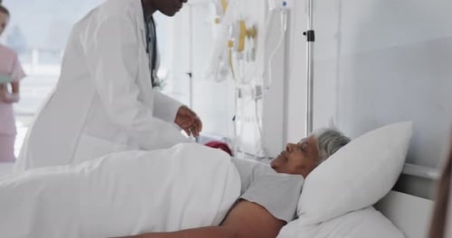 Diverse female doctor checking medication and drip of senior female patient in bed, slow motion
