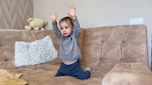 Fröhlicher jubelnder Junge, der auf dem Sofa sitzt. Süßes Kind, das springt, lächelt und aufgeregt mit den Händen winkt
.