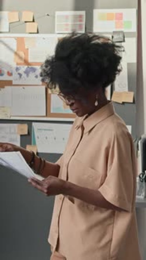 African American Woman Studying Documents At Corkboard In Office