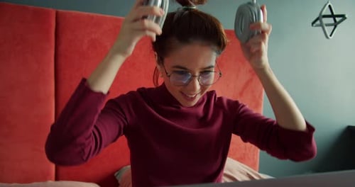 Young Woman Puts on Headphones in Bedroom