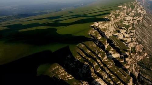 A Majestic Mountain Range Looms Over a Vibrant Green Landscape Its Shadow Dancing Upon the Wild