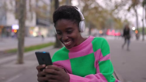 Young Happy Black Woman Having Fun Using Mobile Phone Sitting on City Bench