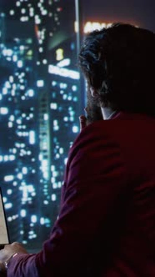 Man Working on Laptop with City Night View