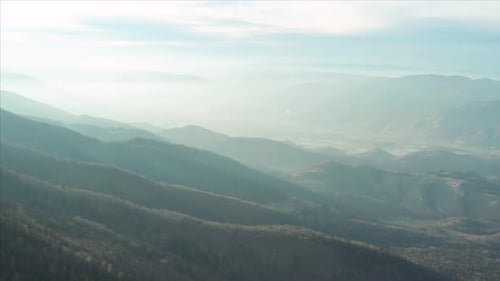 Aerial flyover of a forest-covered mountain range in the morning with fog.