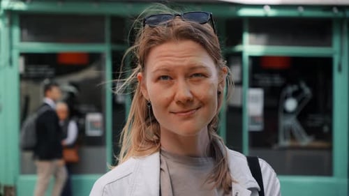 Portrait of Happy Young Woman Looking in Camera in White Jacket with Flowing Hair on Street with