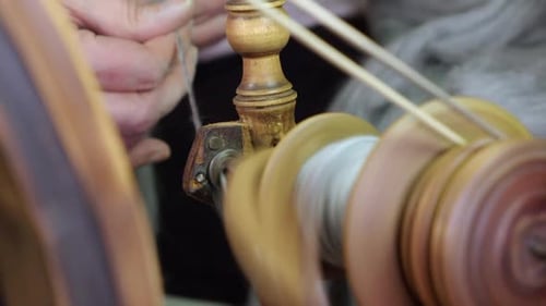 Close up thru bobbin: artisan hands spin wool on Nordic spinning wheel