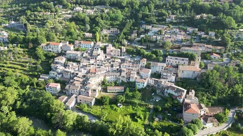 Forward-moving drone footage over a quiet mountain village, revealing winding streets and lush field