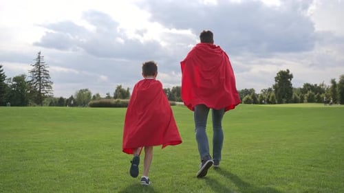 Man and Boy Running in Capes in a Park