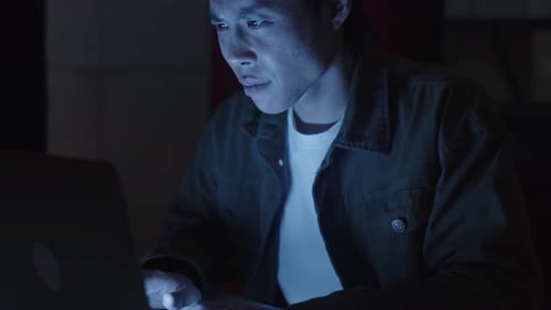 Coder Working on Project Sitting in front of Laptop at Nighttime