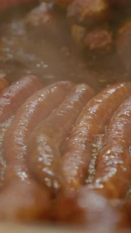 Vertical video Juicy sausages grilling on hot plate at street food market