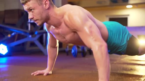 young male shirtless bodybuilder doing push-ups from the floor in a sports club or gym. Strong