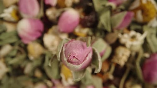 Dry tea made from various herbs and flowers. A rosebud rotates and falls down. Macro slide.