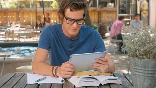 Young Man Uses Tablet at Outdoor Cafe Table