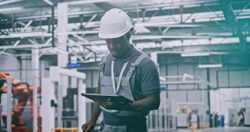 Industrial Male Worker Operating Remote Control System While Overseeing Robots