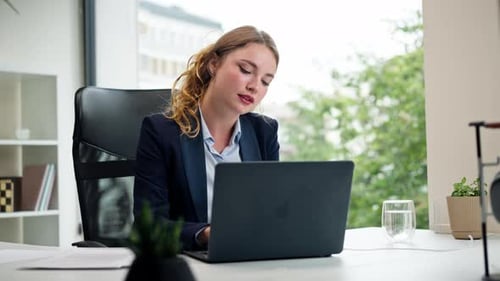 in a Modern Office with a Large Window a Beautiful Worker in a Blue Shirt with a Laptop Looks at the