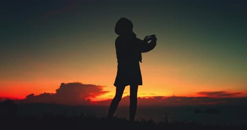 Silhouette of teen photographing a vivid sunset landscape