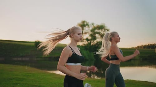 Women Jogging in Meadow near Pond at Sunrise