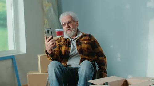 An Elderly Disabled Man in a Wheelchair Talks on a Video Call Using a Mobile Phone