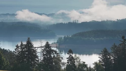 Lush green hills and dense forests surround a calm mountain lake, offering a stunning natural vista,