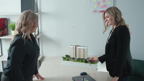 Un agente inmobiliario entrega la llave al cliente y le da la mano con un modelo de construcción sobre la mesa