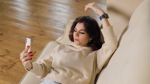 Woman Video Calling on Phone While Relaxing on Couch