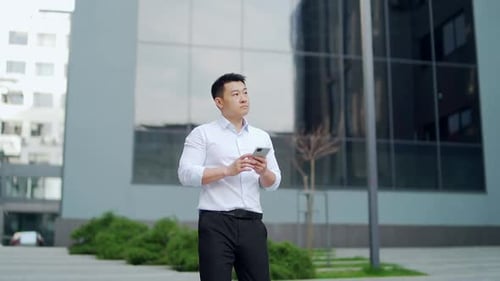 Successful asian business man walks down the city street background of urban office building using