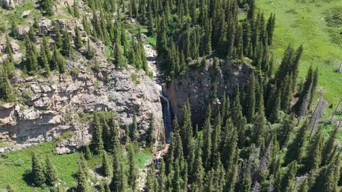 Waterfall Cascading Down Rocky Cliffs in Green Valley