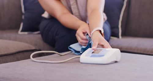 African American woman on sofa unfolding BP cuff while touching monitor on ottoman for BP check
