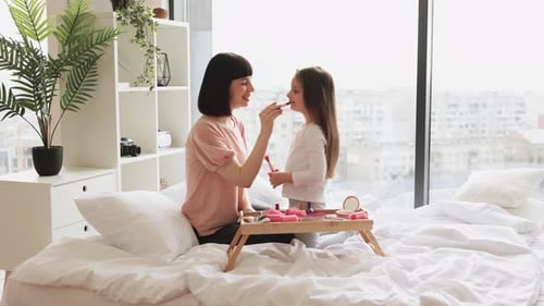 Kleines Mädchen schminkt Mama, die im Schlafzimmer sitzt