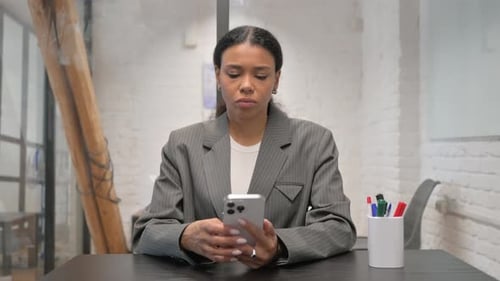 African American Businesswoman Typing Message on Phone at Workspace
