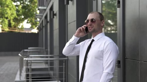 Businessman speaks on the phone near the office outdoors.