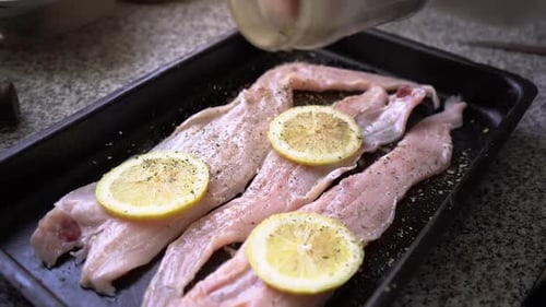 Sprinkling Spices On Fresh Hake Fish Fillet With Lemon Slices In A Baking Pan. close up, slow motion