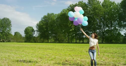 Happy Woman Jumps with Balloons in Grassy Field