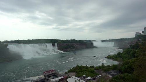 Panoramic view of Niagara Falls, water flowing down the waterfall creating steam, on a cloudy day