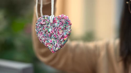 Woman Arranging Vibrant Handmade Heart Ornament Amid Indoor Garden Ambiance During Morning Light